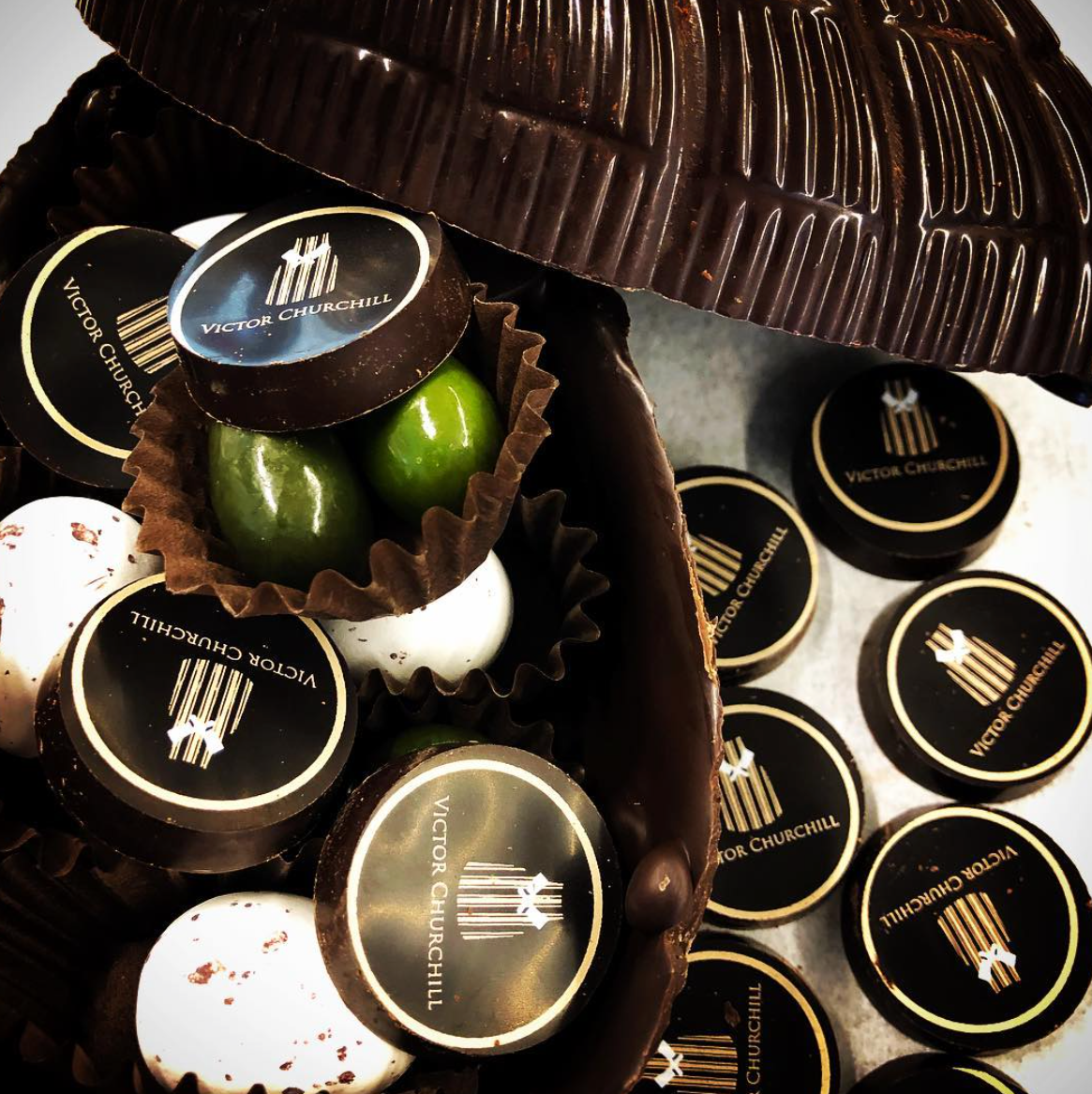 Artisan handmade chocolate truffles with dark shells and green centers, arranged beside round wrapped chocolates.