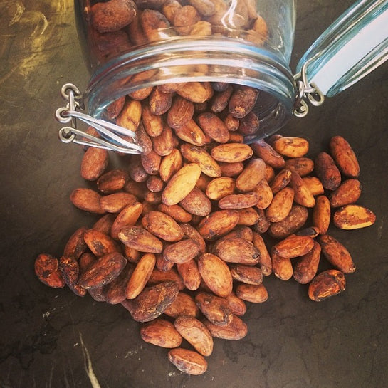 artisan handmade chocolate-coated nuts spill from a clear glass jar onto a dark surface