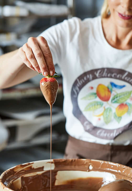 Artisan handmade chocolate pours in a thin stream over dessert in a kitchen bowl.