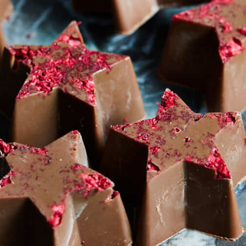 Artisan handmade chocolate bars with red sprinkles, stacked on a dark surface in close-up
