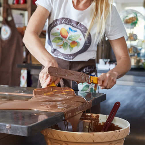 Artisan handmade chocolate bars melt in a glass tempering machine as a baker breaks a chunk