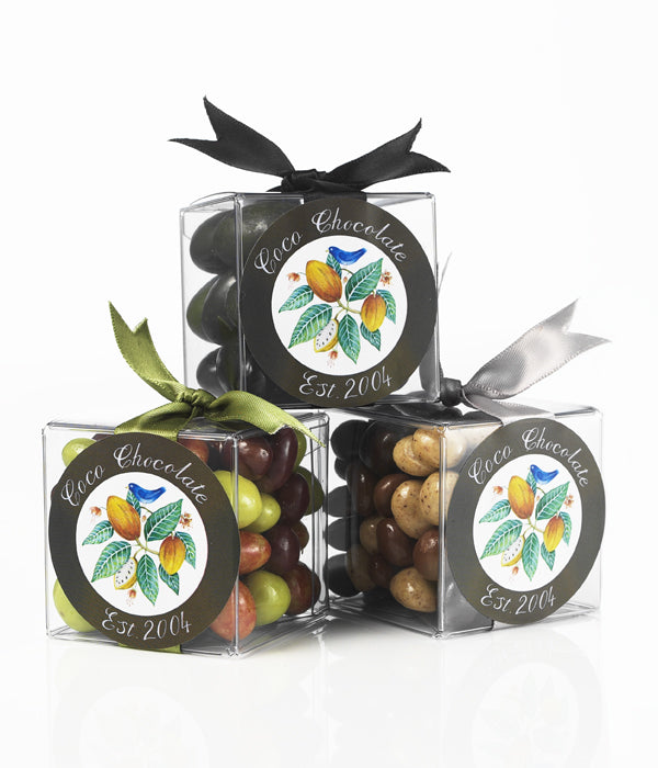 Artisan handmade chocolate truffles in clear boxes with round labels showing cocoa, dark and green pieces.