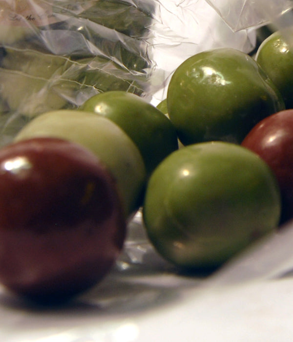 Handmade chocolate truffles in deep green and dark red—artisan pieces, glossy and rounded.