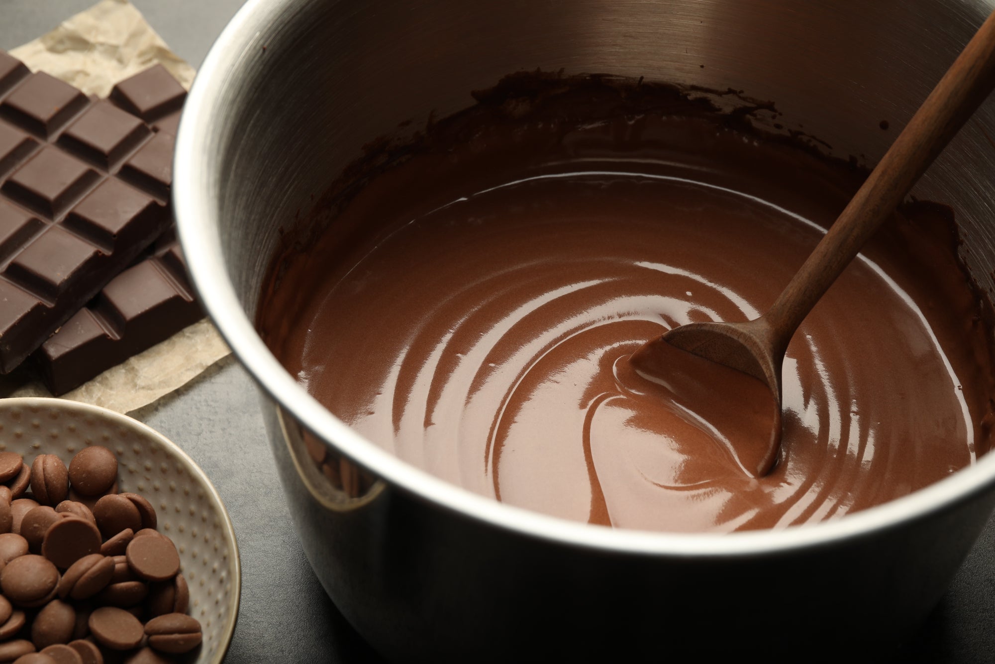 Artisan handmade chocolate in a mixing bowl, spoon stirring dark brown swirl beside chocolate bars.