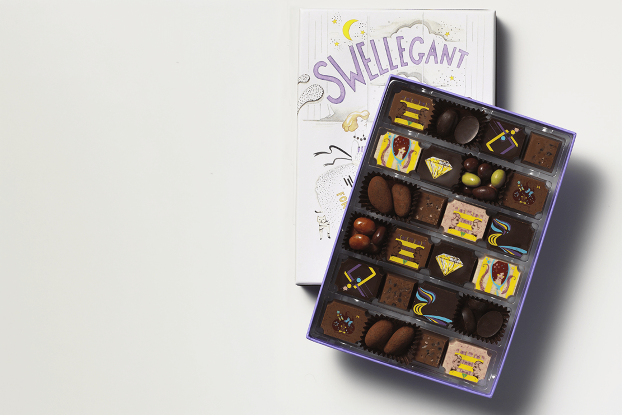 An artisan handmade chocolate assortment sits in an open box, showing various molded pieces